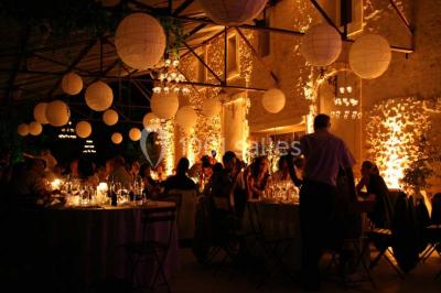 Salle de réception avec une longue table dressée, nappes blanches, vaisselle élégante et décorations florales.