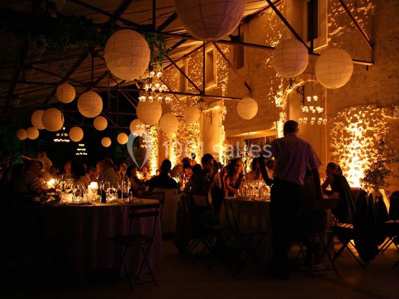 Salle de réception éclairée par des lanternes suspendues, avec des invités assis à des tables décorées.