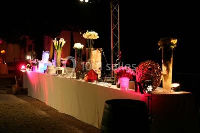 Salle de réception avec une longue table dressée, nappes blanches, vaisselle élégante et décorations florales.