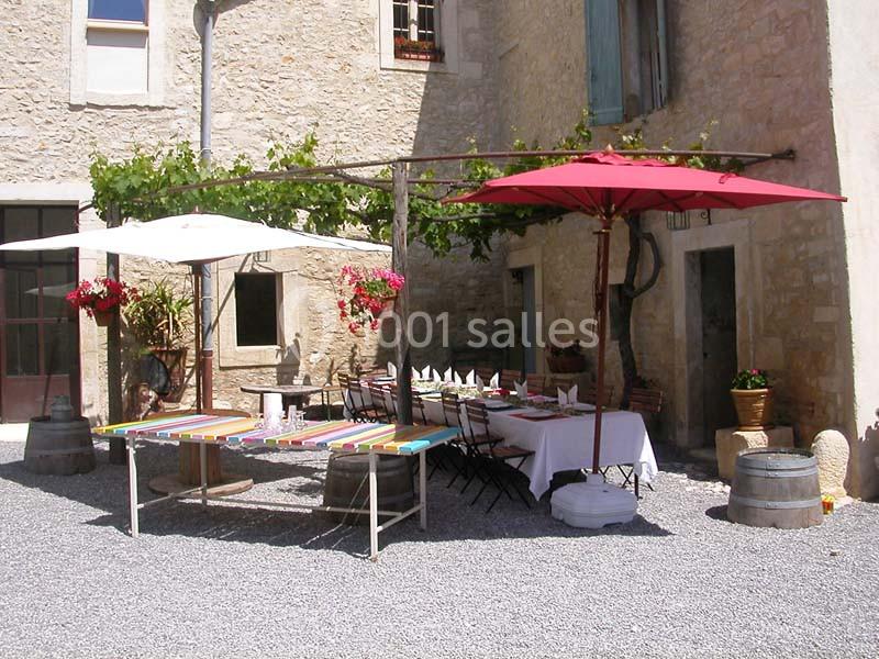 Cour ensoleillée avec tables dressées sous des parasols colorés, entourée de murs en pierre et de plantes fleuries.
