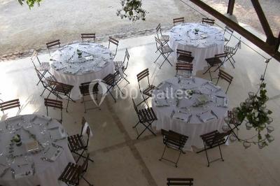 Salle de réception avec une longue table dressée, nappes blanches, vaisselle élégante et décorations florales.