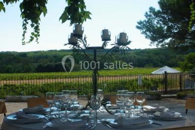Salle de réception avec une longue table dressée, nappes blanches, vaisselle élégante et décorations florales.