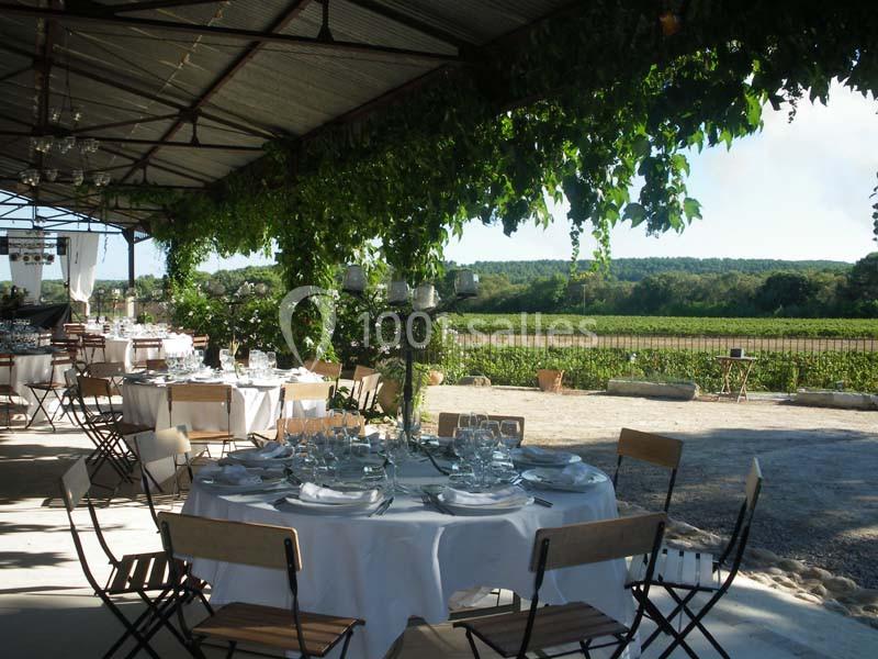 Salle de réception en plein air avec tables dressées sous une pergola, vue sur un paysage champêtre verdoyant.