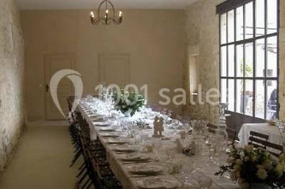 Salle de réception avec une longue table dressée, nappes blanches, vaisselle élégante et décorations florales.