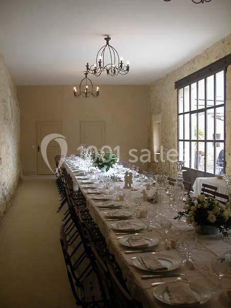 Salle de réception avec une longue table dressée, nappes blanches, vaisselle élégante et décorations florales.