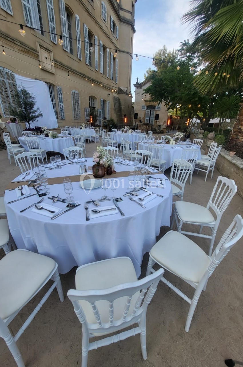 Tables rondes dressées avec nappes blanches et chaises, disposées en extérieur devant un bâtiment ancien.