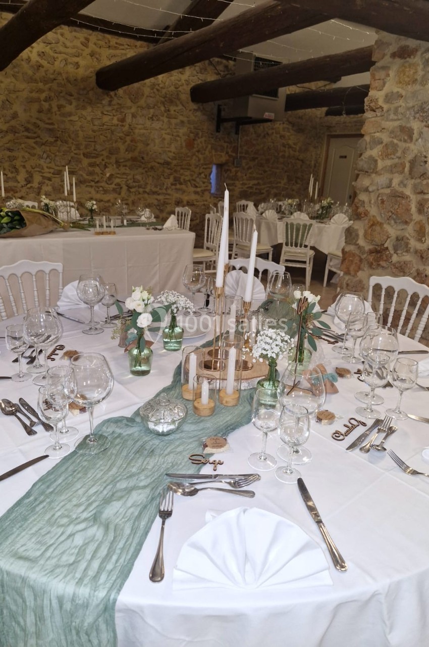 Table de réception élégamment dressée avec nappes blanches, décoration florale et bougies dans une salle en pierre.