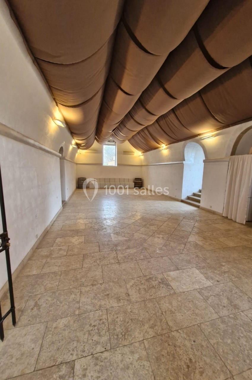 Salle voûtée avec un plafond en tissu tendu, murs blancs, sol en pierre et lumière douce.