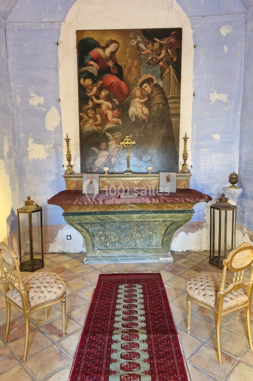 Autel ancien avec tableau religieux, croix dorée, chandeliers et deux chaises dans une petite chapelle aux murs patinés.