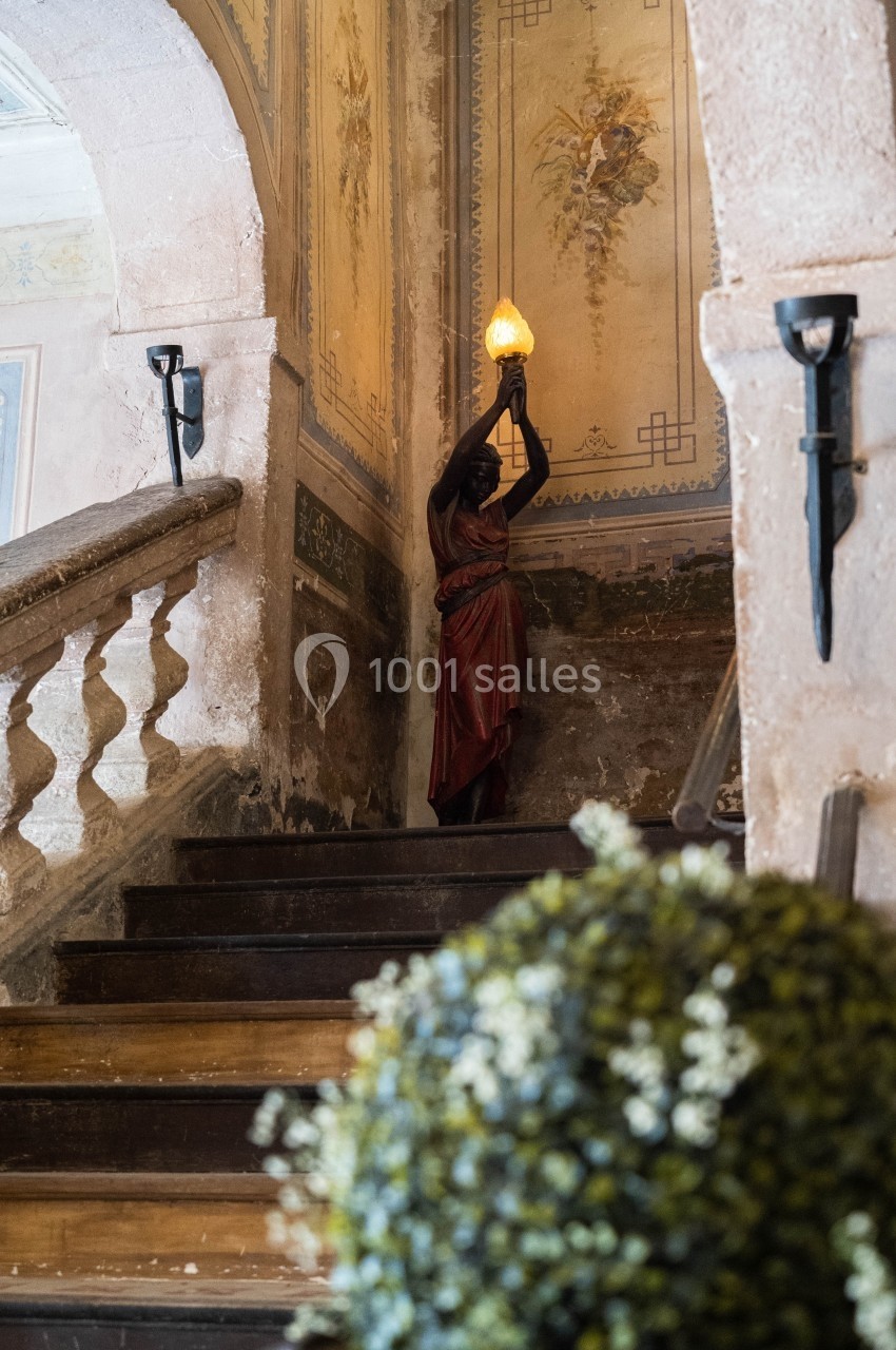 Escalier ancien avec une statue tenant une lampe, entouré de murs décorés et d'une rampe en pierre.