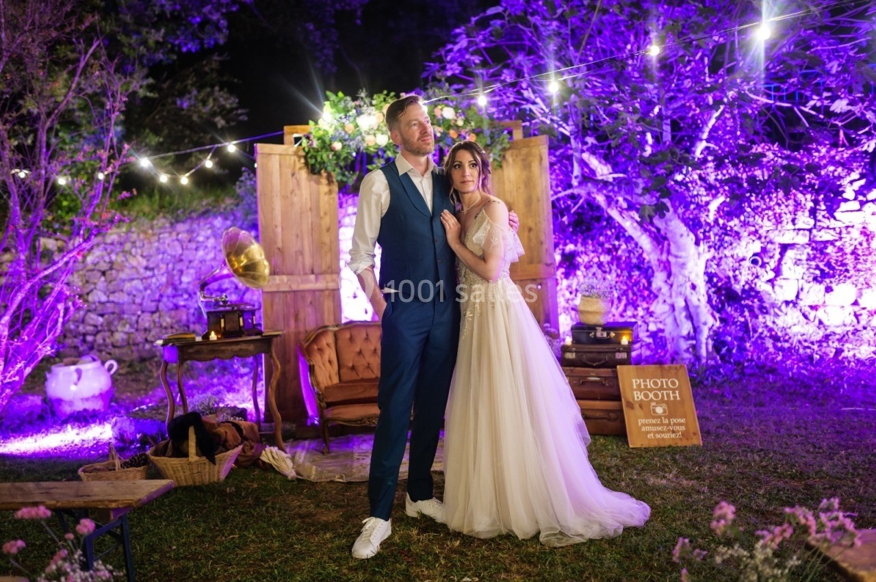 Un couple pose devant une décoration lumineuse de mariage en extérieur, avec un coin photo aménagé.