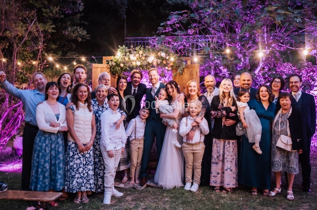Groupe de personnes posant ensemble dans un jardin décoré de guirlandes lumineuses, ambiance festive en soirée.