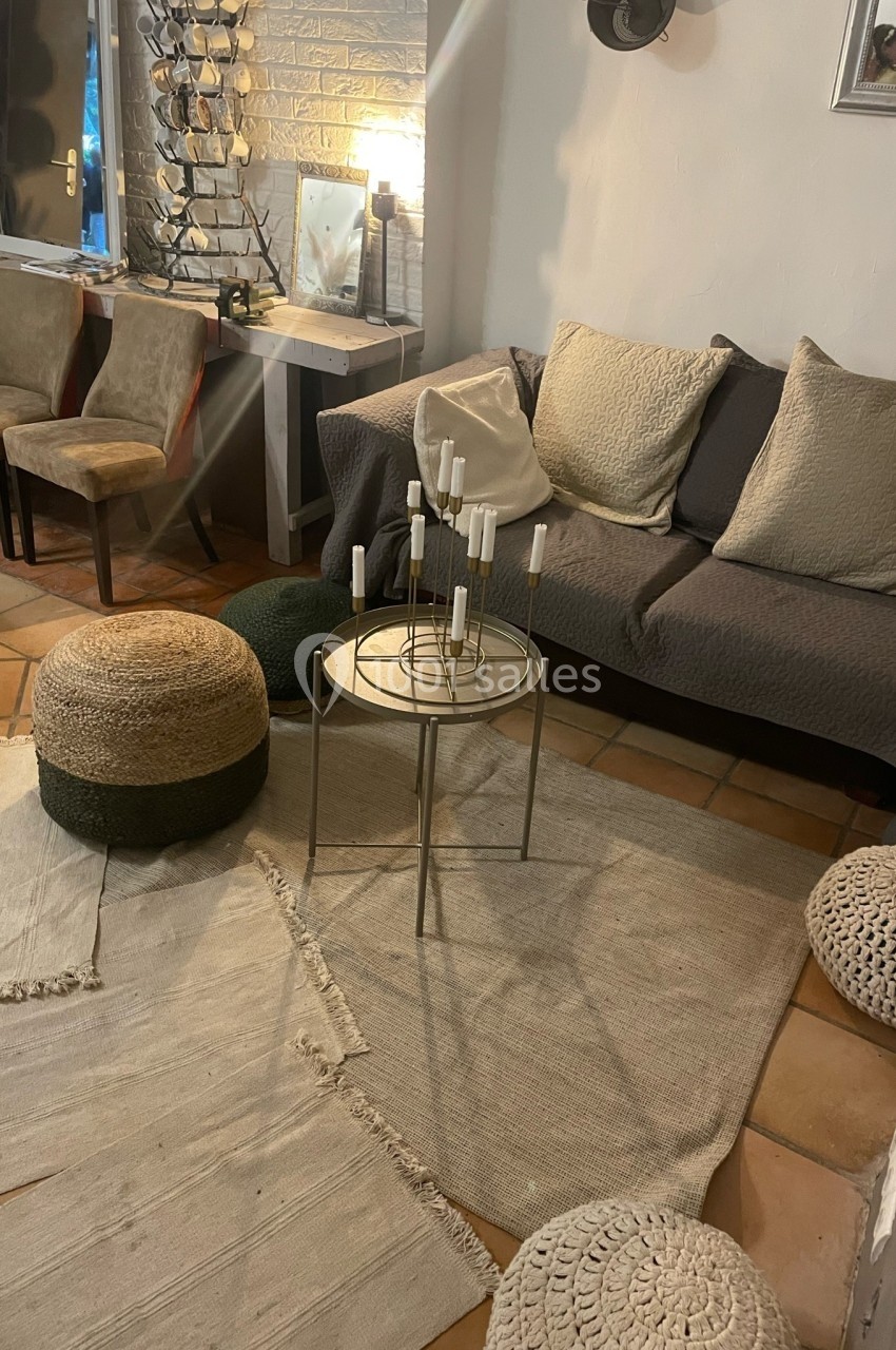 Salon cosy avec canapé gris, table basse ronde avec bougies, poufs en osier et tapis clairs sur sol en terre cuite.