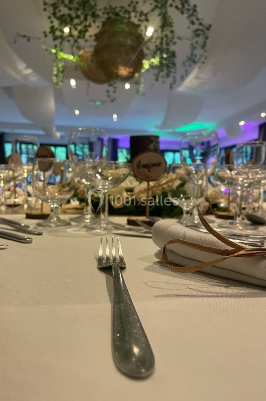 Table élégamment dressée avec des couverts, verres et décorations végétales suspendues dans une salle éclairée.