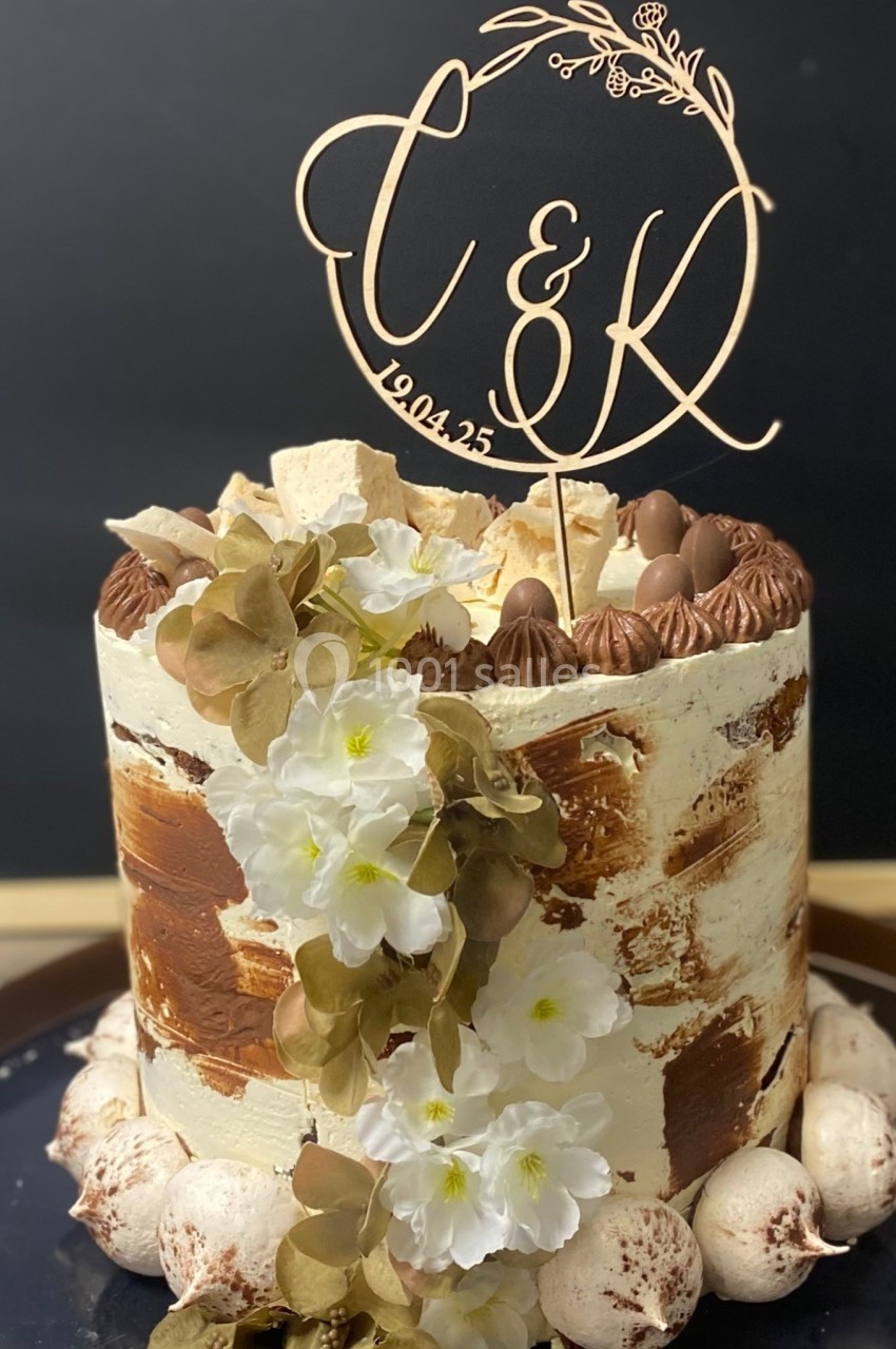 Gâteau décoré de fleurs blanches, de meringues et d'un cake topper personnalisé avec des initiales et une date.