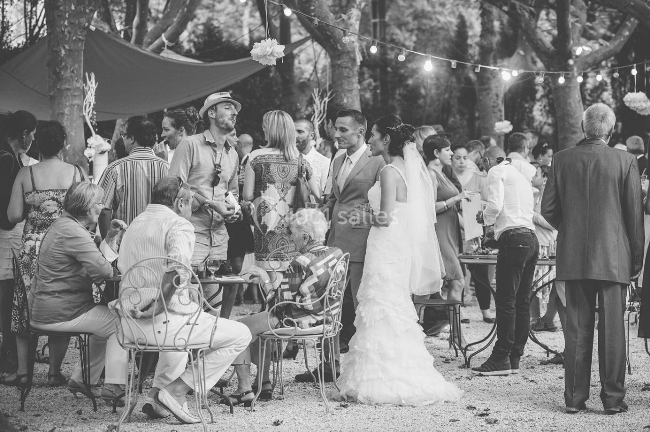 Groupe de personnes rassemblées lors d'une réception en extérieur, avec des guirlandes lumineuses et des arbres en arrière…