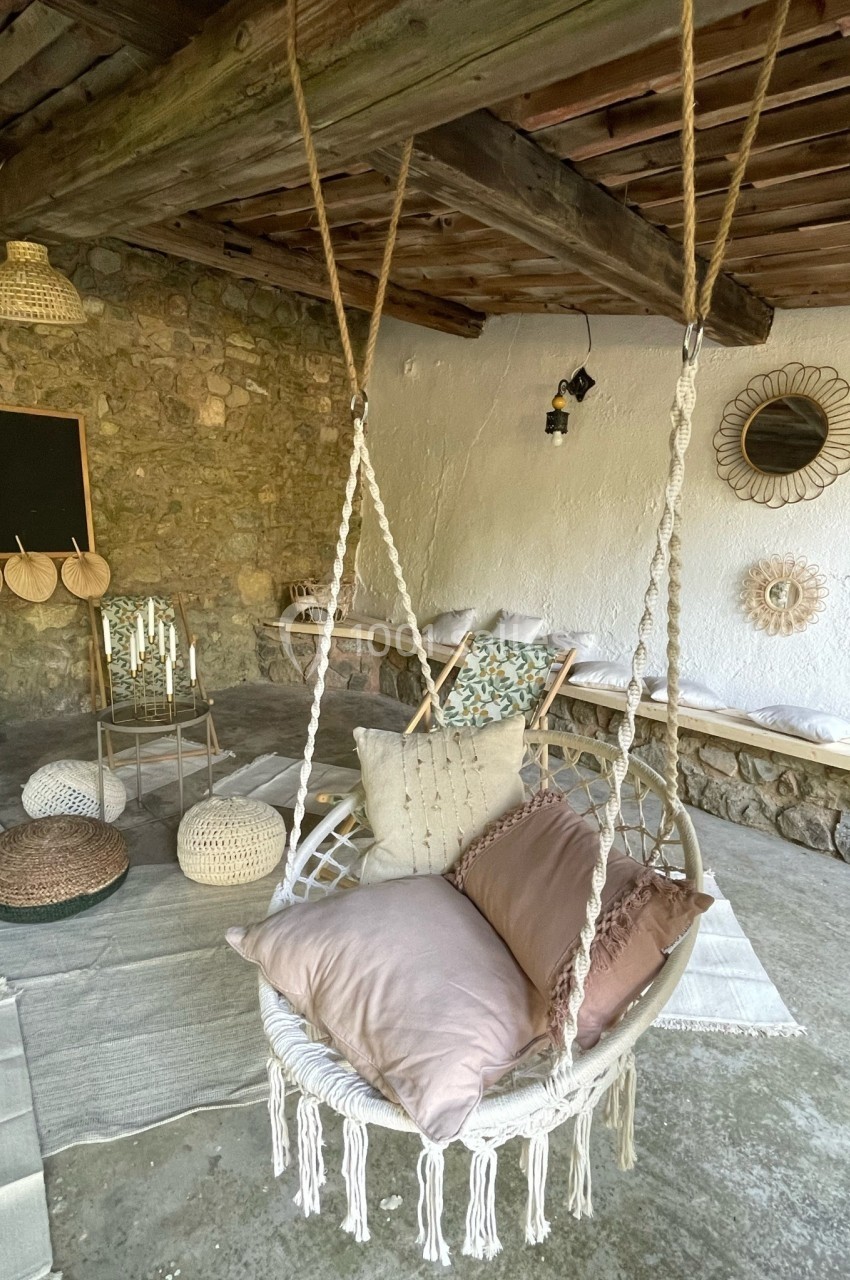 Fauteuil suspendu en corde avec coussins, dans un espace extérieur décoré de tapis, poufs et éléments en rotin.