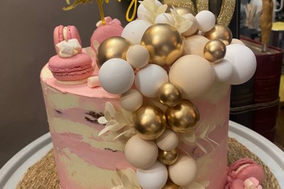 Gâteau d'anniversaire rose décoré de macarons, ballons comestibles dorés et blancs, avec un topper ’Happy Birthday 30’.