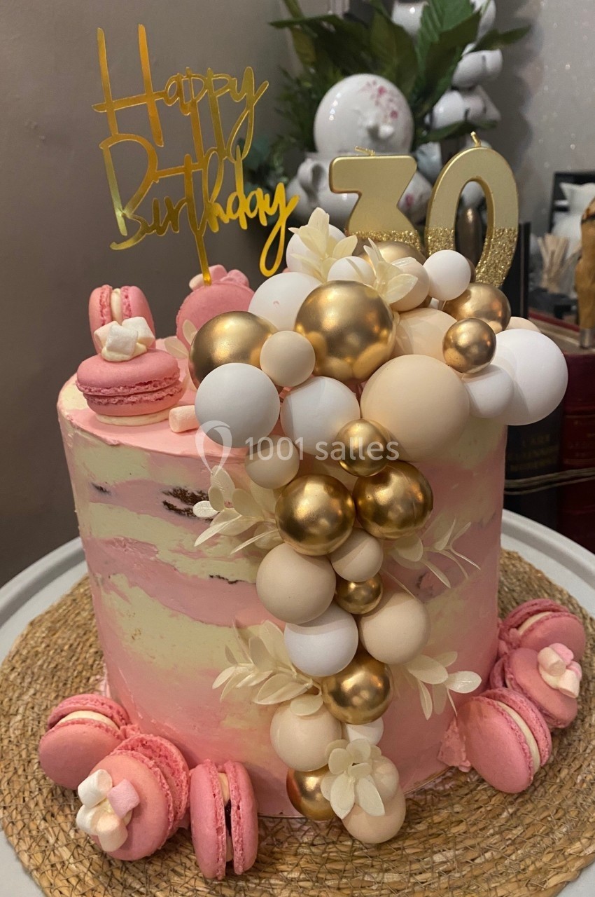 Gâteau d'anniversaire rose décoré de macarons, ballons comestibles dorés et blancs, avec un topper ’Happy Birthday 30’.