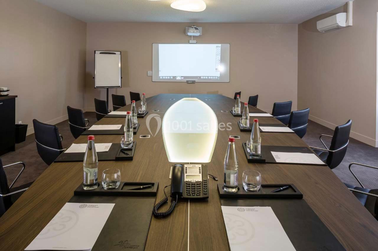 Salle de réunion équipée d'une grande table ovale, chaises, téléphone, bouteilles d'eau et tableau interactif.