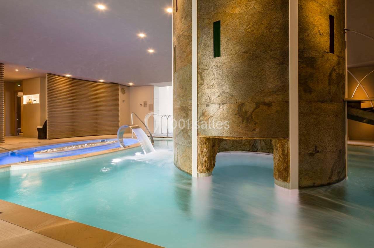 Piscine intérieure avec jets d'eau, bain à remous et colonne en pierre dans un espace lumineux et moderne.