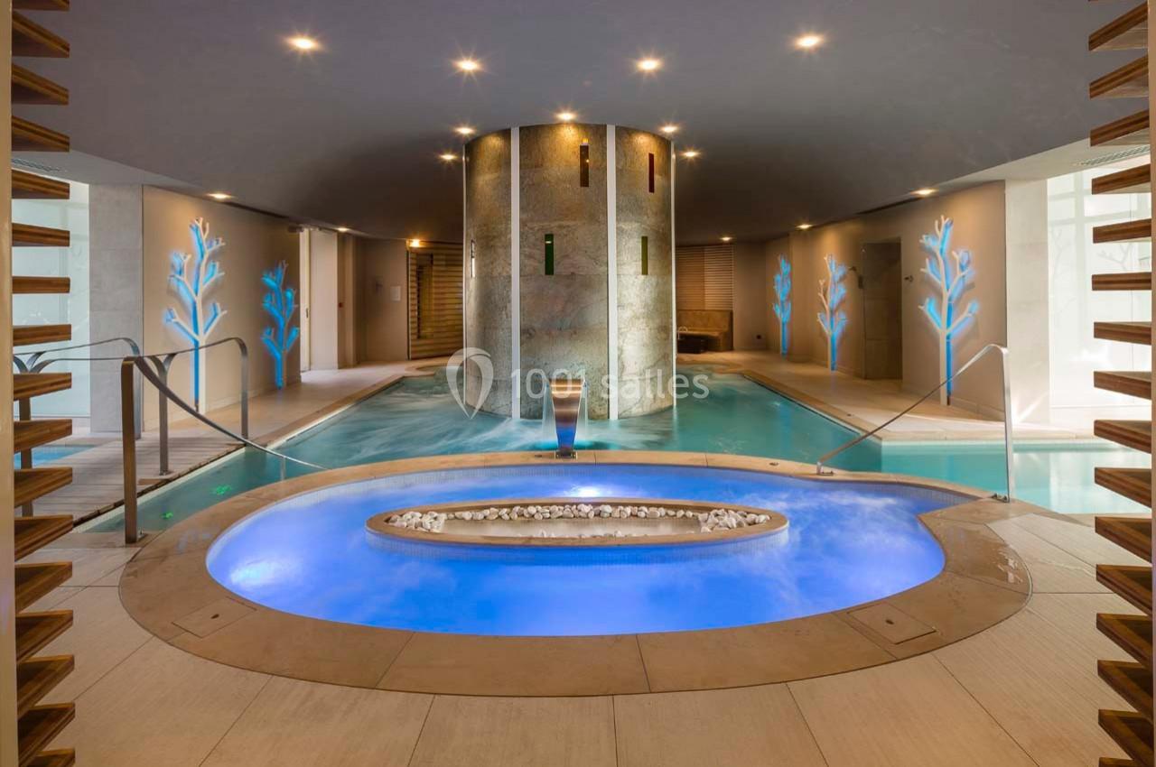 Piscine intérieure avec bain à remous éclairé en bleu, entourée de décorations murales lumineuses et d'un pilier central.