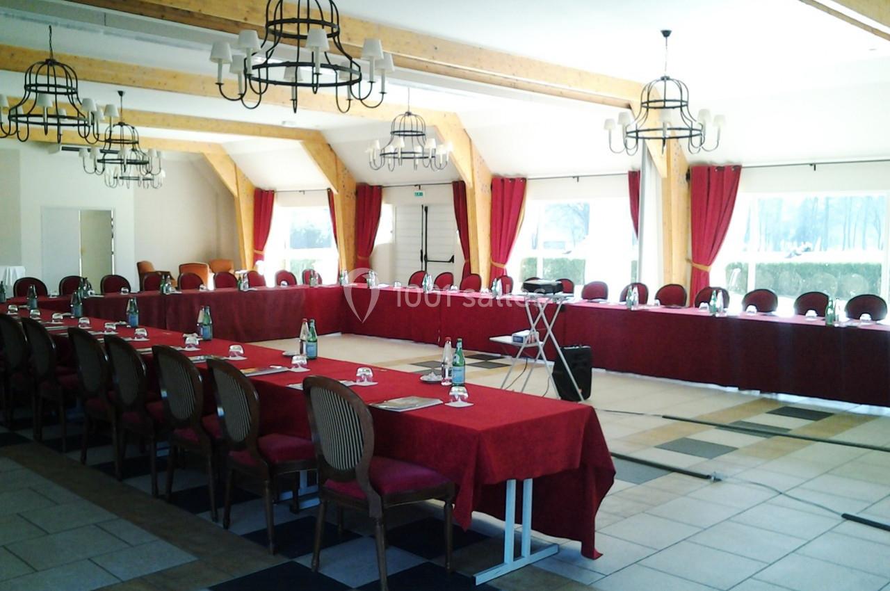 Salle de réunion lumineuse avec de longues tables rouges, des chaises en bois et des lustres suspendus.