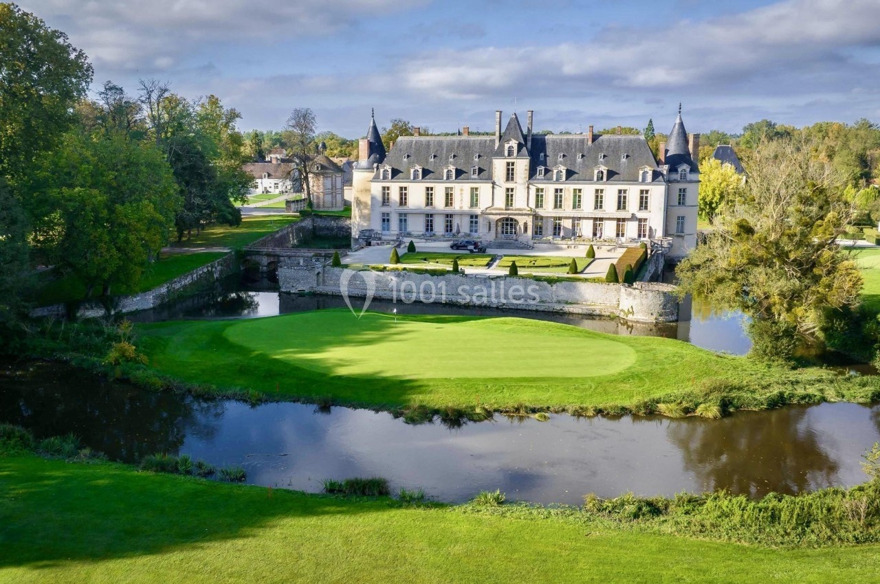 Château entouré de jardins verdoyants, bordé par une rivière sous un ciel partiellement nuageux.