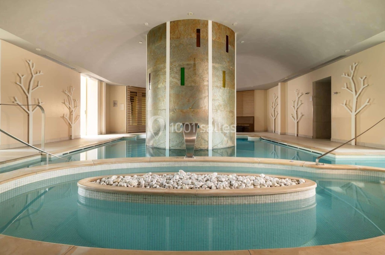 Piscine intérieure avec jets d'eau, décorée de pierres blanches et entourée de murs ornés de motifs d'arbres.