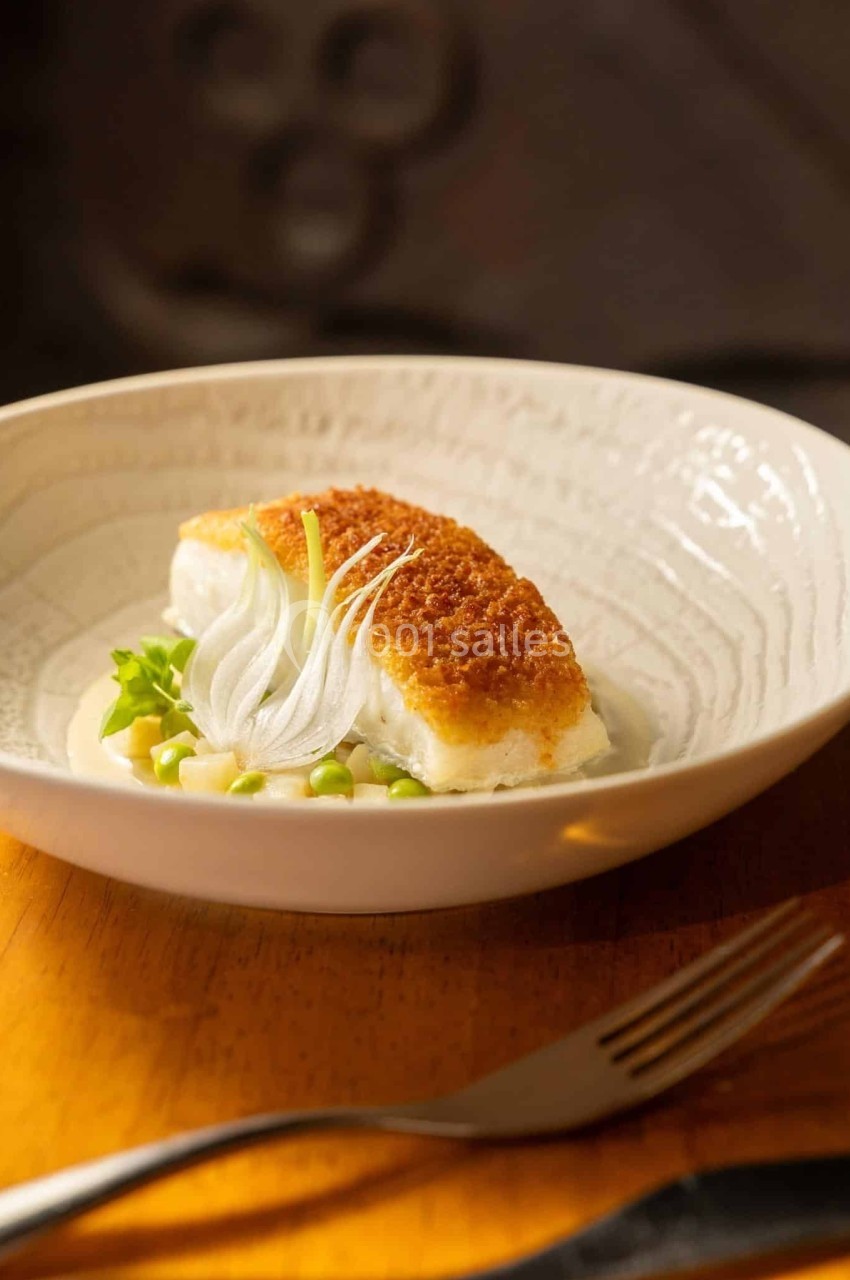 Filet de poisson pané servi sur une sauce crémeuse avec petits pois, oignons émincés et herbes fraîches dans une assiette…