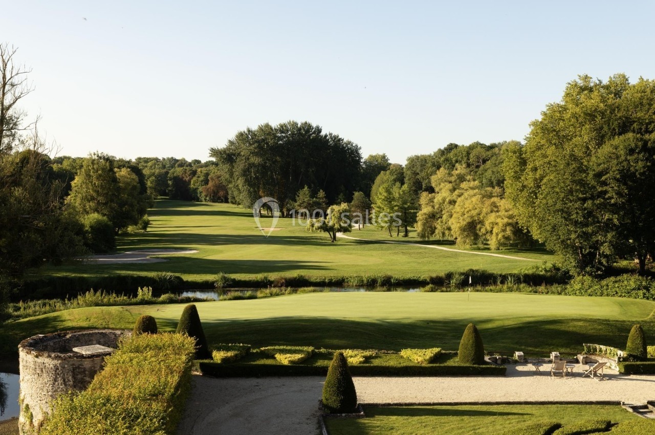 Vue d'un terrain de golf verdoyant entouré d'arbres, avec un jardin aménagé au premier plan.