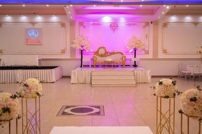 Salle de réception décorée avec un canapé doré, des arbres fleuris et un éclairage rose sur une estrade blanche.