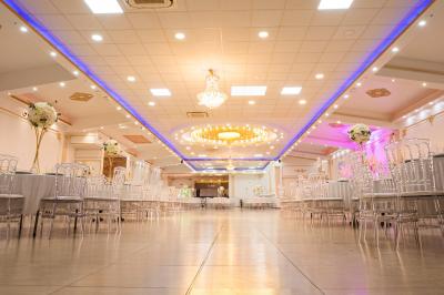 Salle de réception décorée avec un canapé doré, des arbres fleuris et un éclairage rose sur une estrade blanche.