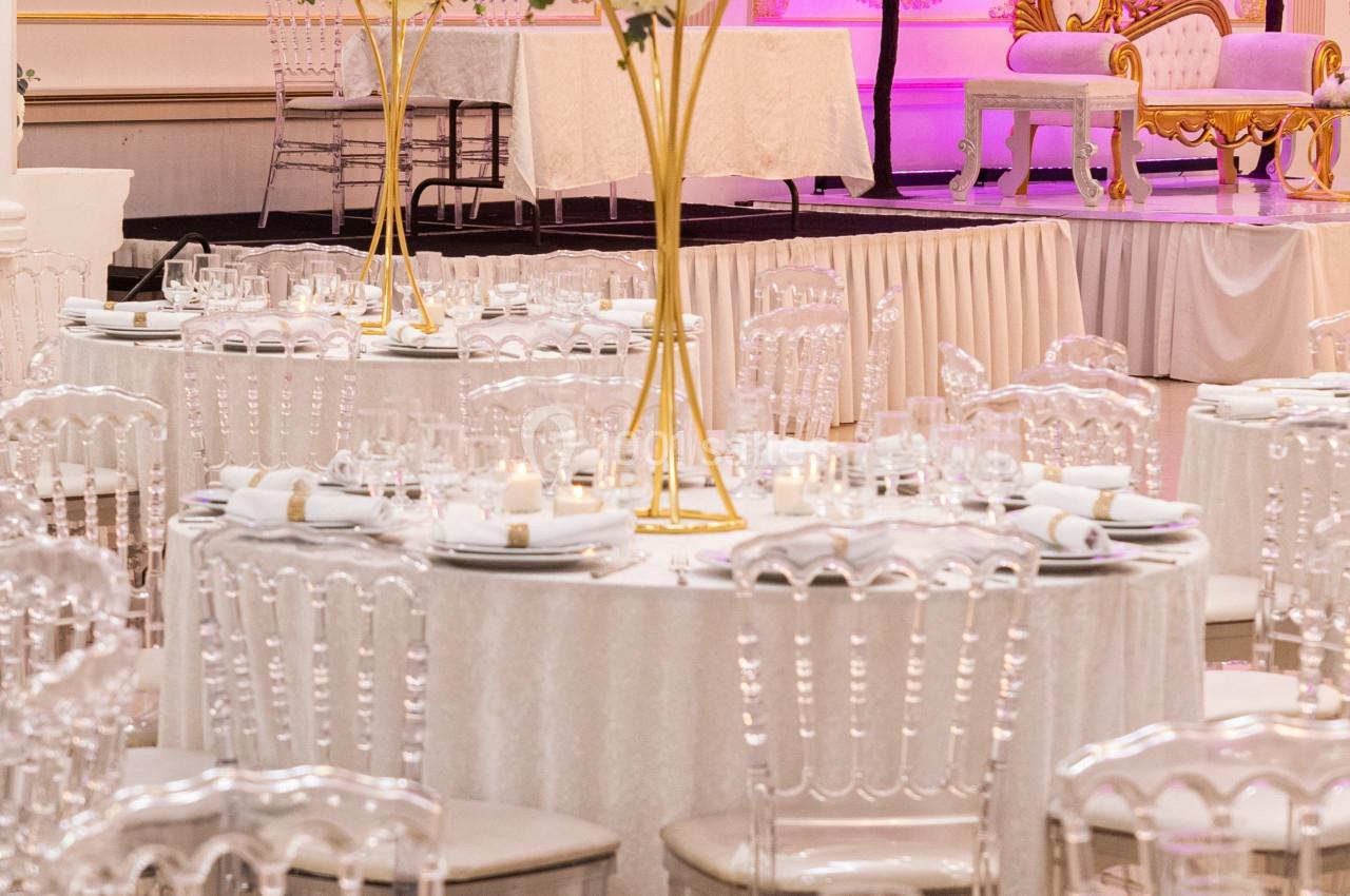 Salle de réception élégante avec tables rondes décorées de nappes blanches, chandeliers et fleurs, éclairage rose en arrière…