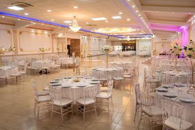 Salle de réception décorée avec un canapé doré, des arbres fleuris et un éclairage rose sur une estrade blanche.