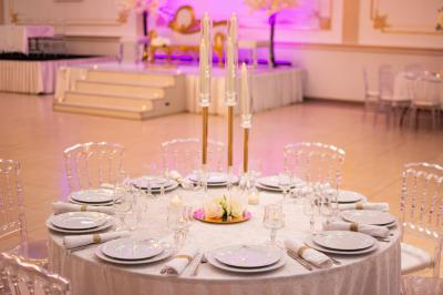 Salle de réception décorée avec un canapé doré, des arbres fleuris et un éclairage rose sur une estrade blanche.