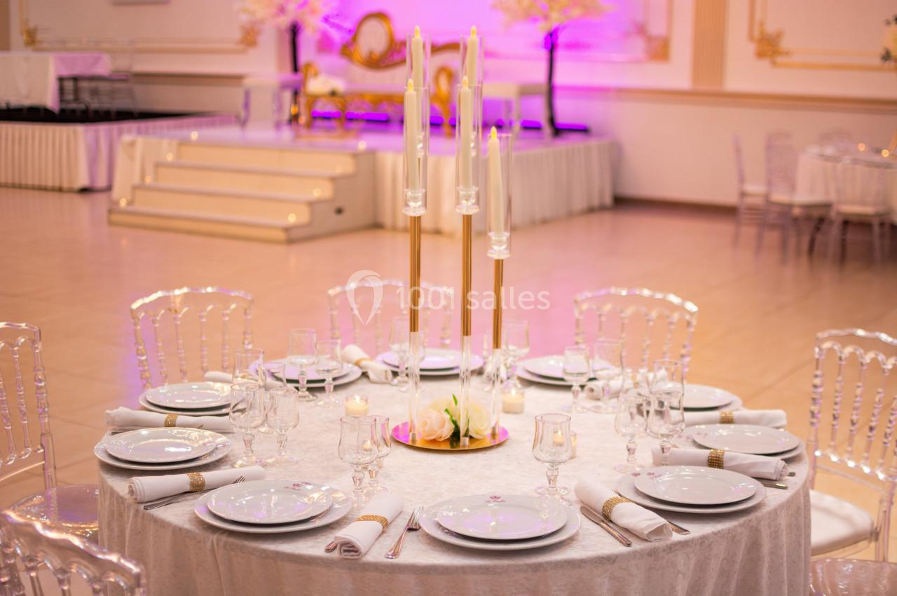 Table élégamment dressée avec des assiettes blanches, des verres et un centre de table à bougies dans une salle de réception.