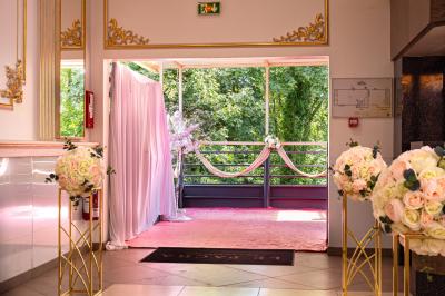 Salle de réception décorée avec un canapé doré, des arbres fleuris et un éclairage rose sur une estrade blanche.