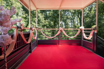 Salle de réception décorée avec un canapé doré, des arbres fleuris et un éclairage rose sur une estrade blanche.