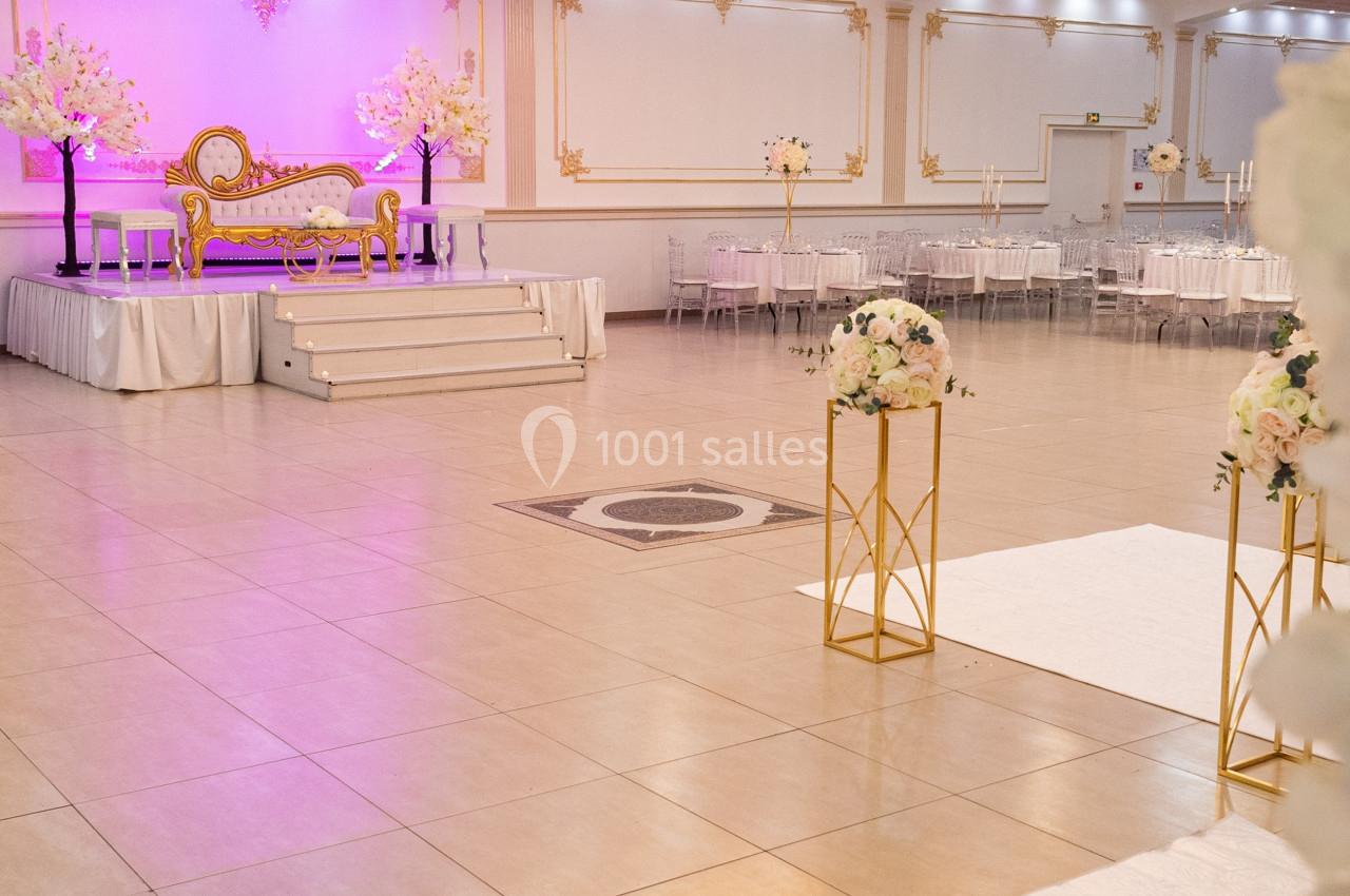 Salle de réception décorée avec un lustre central, une scène ornée d'un canapé doré et des arrangements floraux.