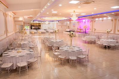 Salle de réception décorée avec un canapé doré, des arbres fleuris et un éclairage rose sur une estrade blanche.