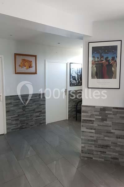 Un couloir intérieur avec murs carrelés gris, portes blanches et cadres décoratifs accrochés aux murs.