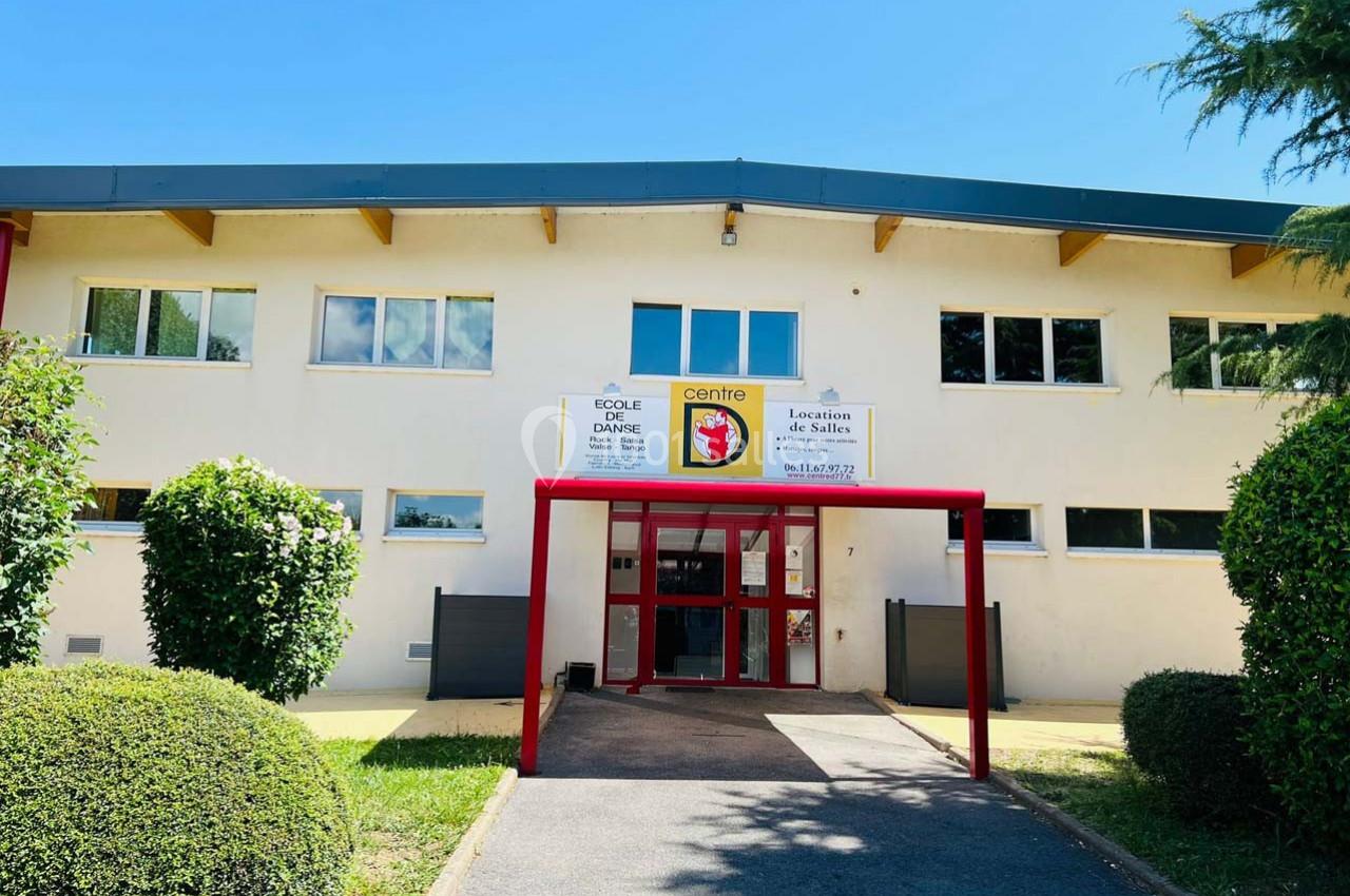 Façade d'un bâtiment avec entrée principale rouge, entourée de verdure et sous un ciel dégagé.