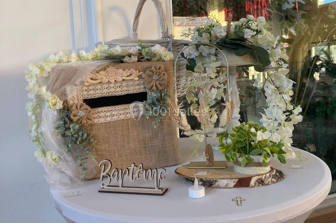 Décoration de table pour un baptême avec urne en toile de jute, fleurs blanches et accessoires religieux.
