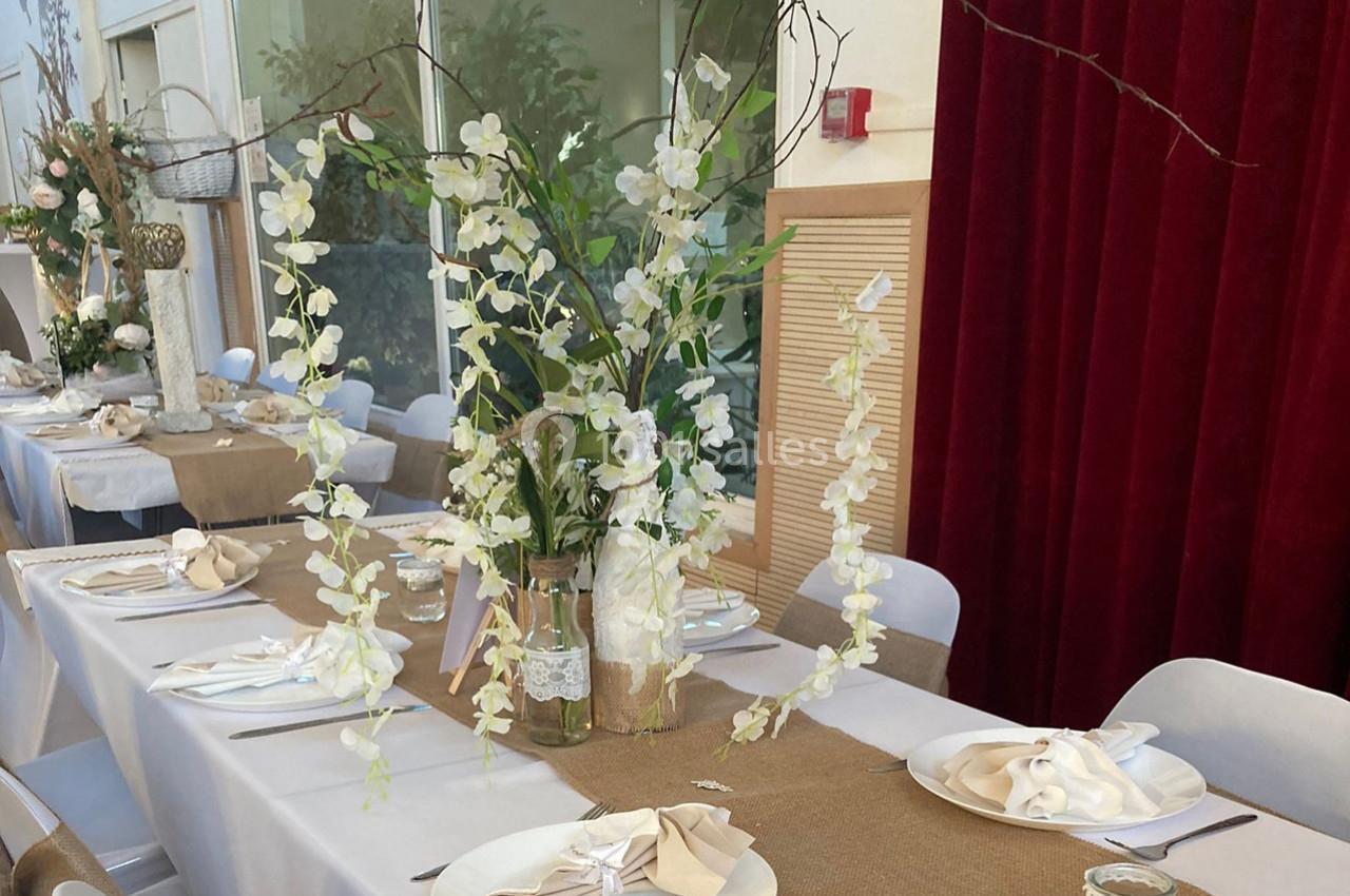 Décoration de table avec nappes blanches, chemins de table en toile de jute et un vase d'orchidées blanches.