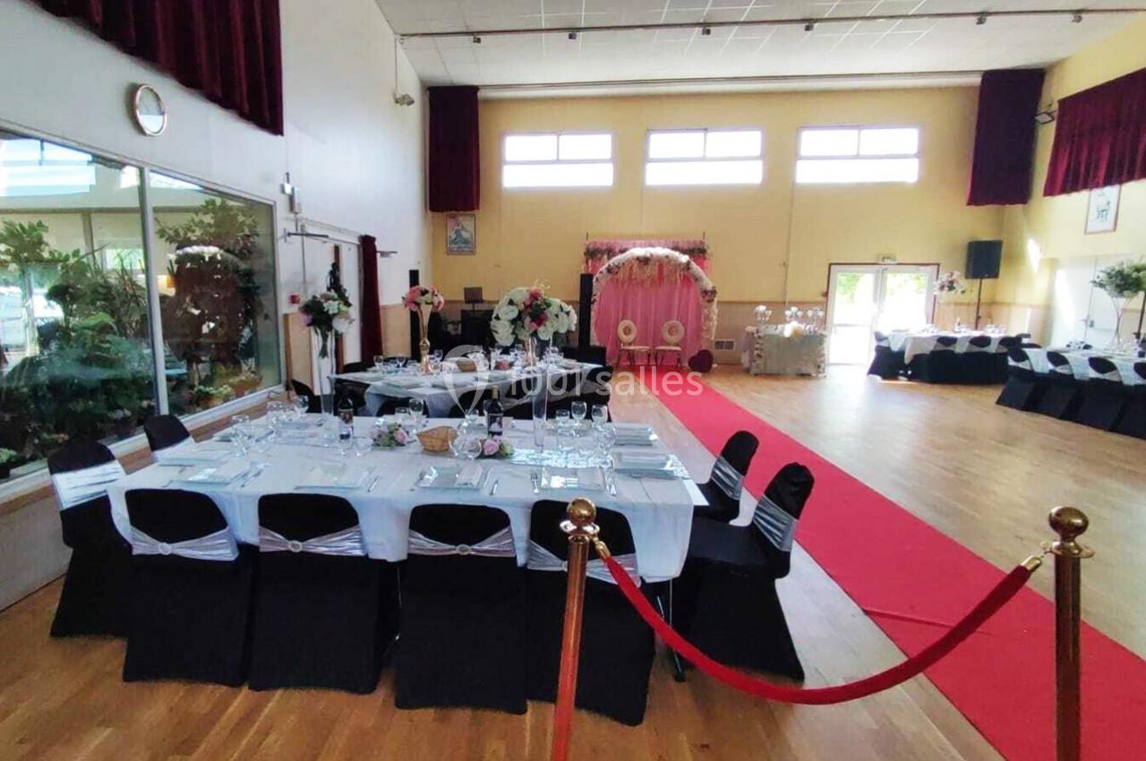 Salle de réception décorée pour un événement, avec tables dressées, allée rouge et arche fleurie au fond.