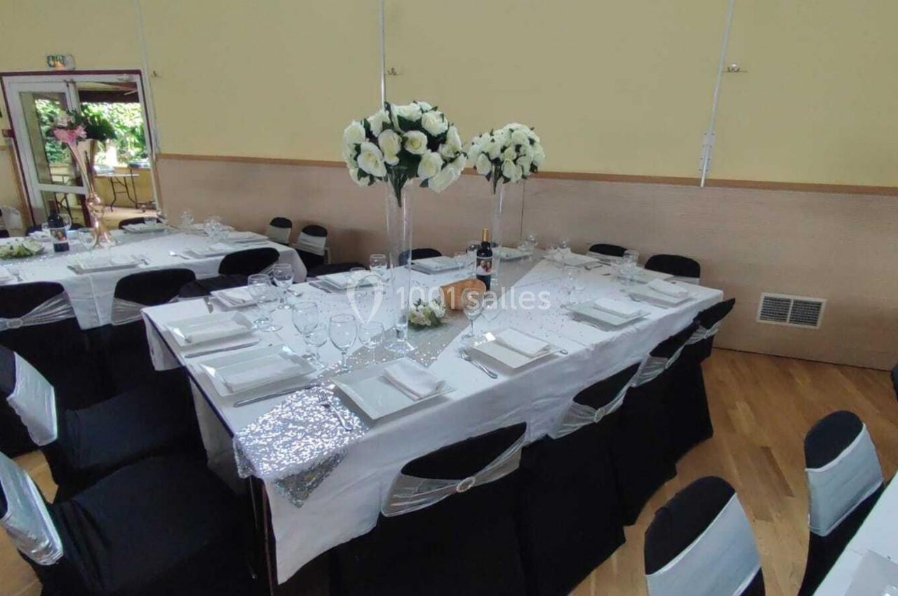 Table de réception décorée avec nappes blanches, chaises noires, centres de table fleuris et vaisselle élégante.