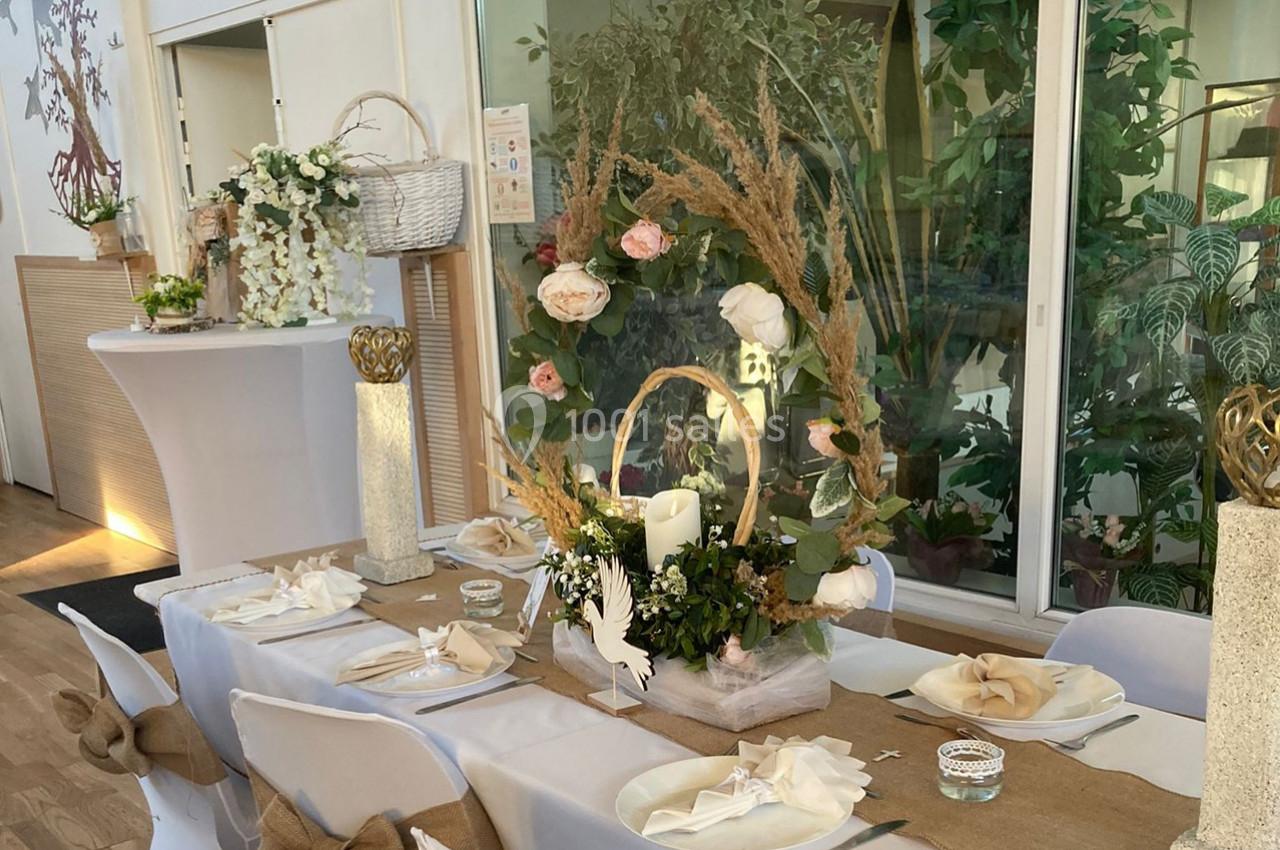 Table décorée pour un événement avec des fleurs, des bougies et des éléments naturels dans une salle lumineuse.