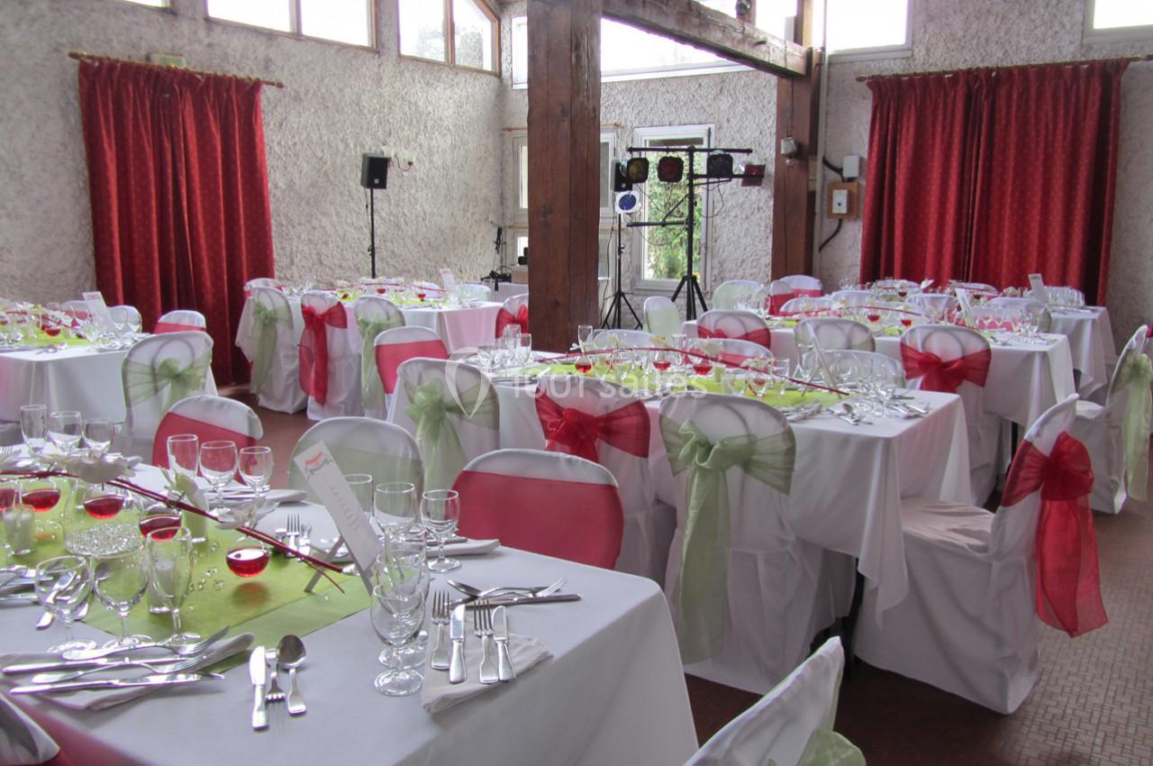 Salle de réception décorée avec des nappes blanches, des rubans colorés sur les chaises et des tables dressées.