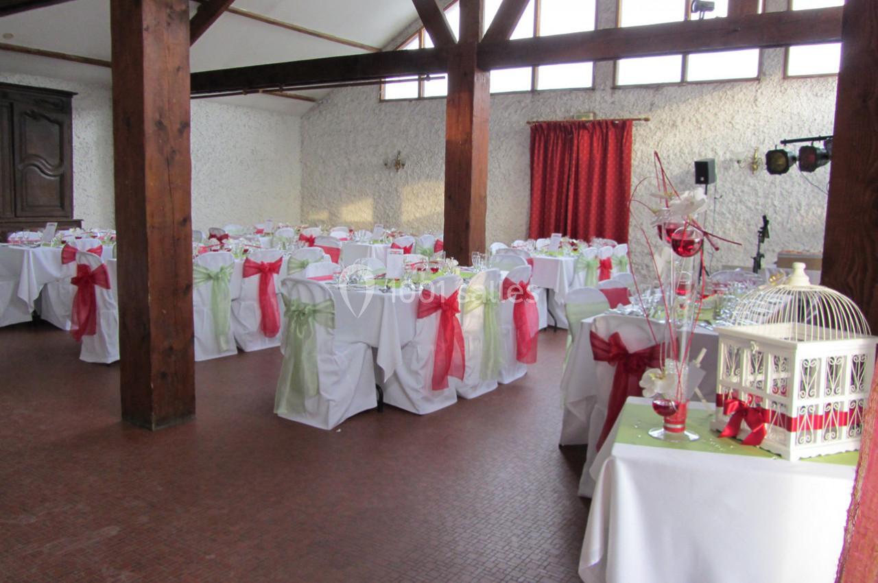 Salle de réception décorée avec des tables nappées de blanc, ornées de nœuds rouges et verts, sous une charpente en bois.